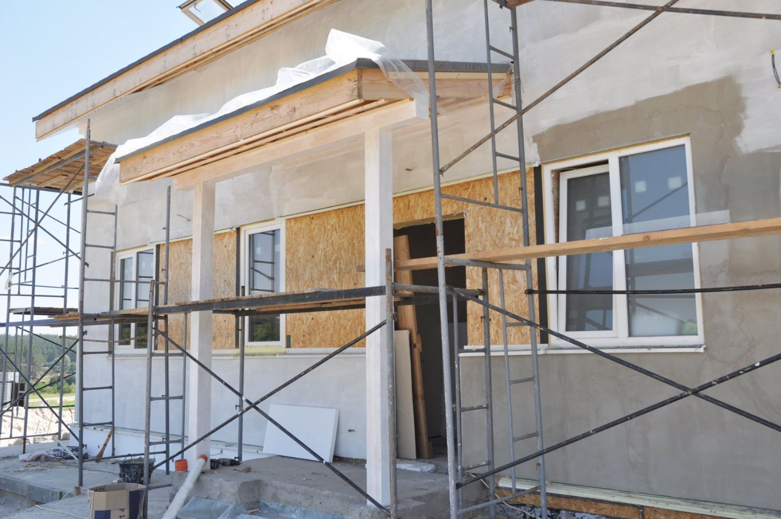 Modern house under construction with scaffolding, white walls, and wooden window frames