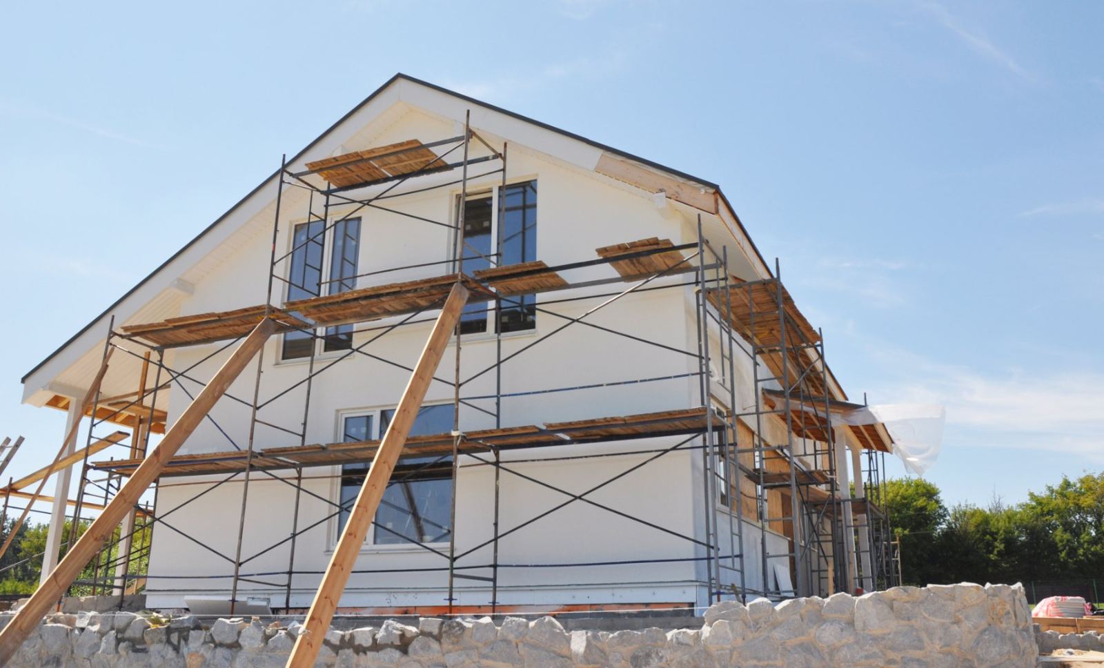 Two-story house under construction with wooden scaffolding and white exterior walls