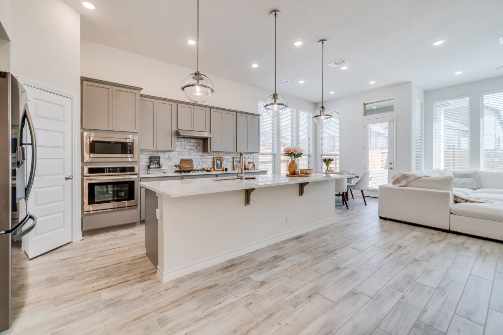 Modern open-concept kitchen with white island, gray cabinetry, stainless steel appliances, and pendant lighting