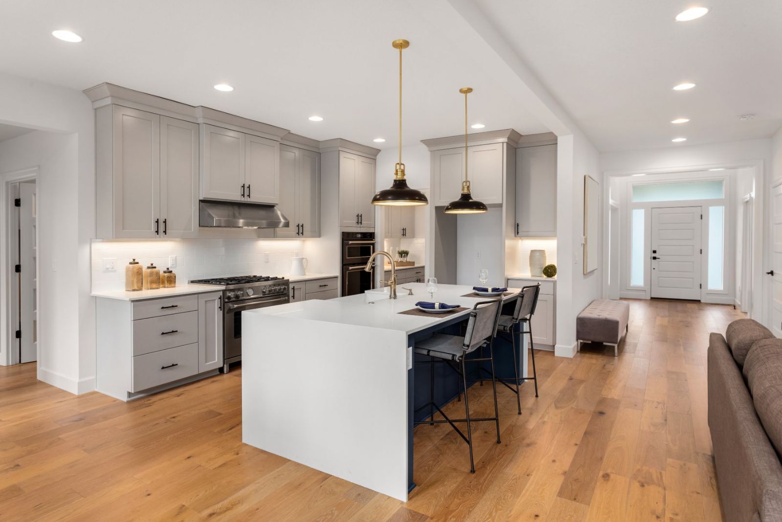 Modern kitchen with gray cabinetry, white island, black pendant lights, and wooden flooring
