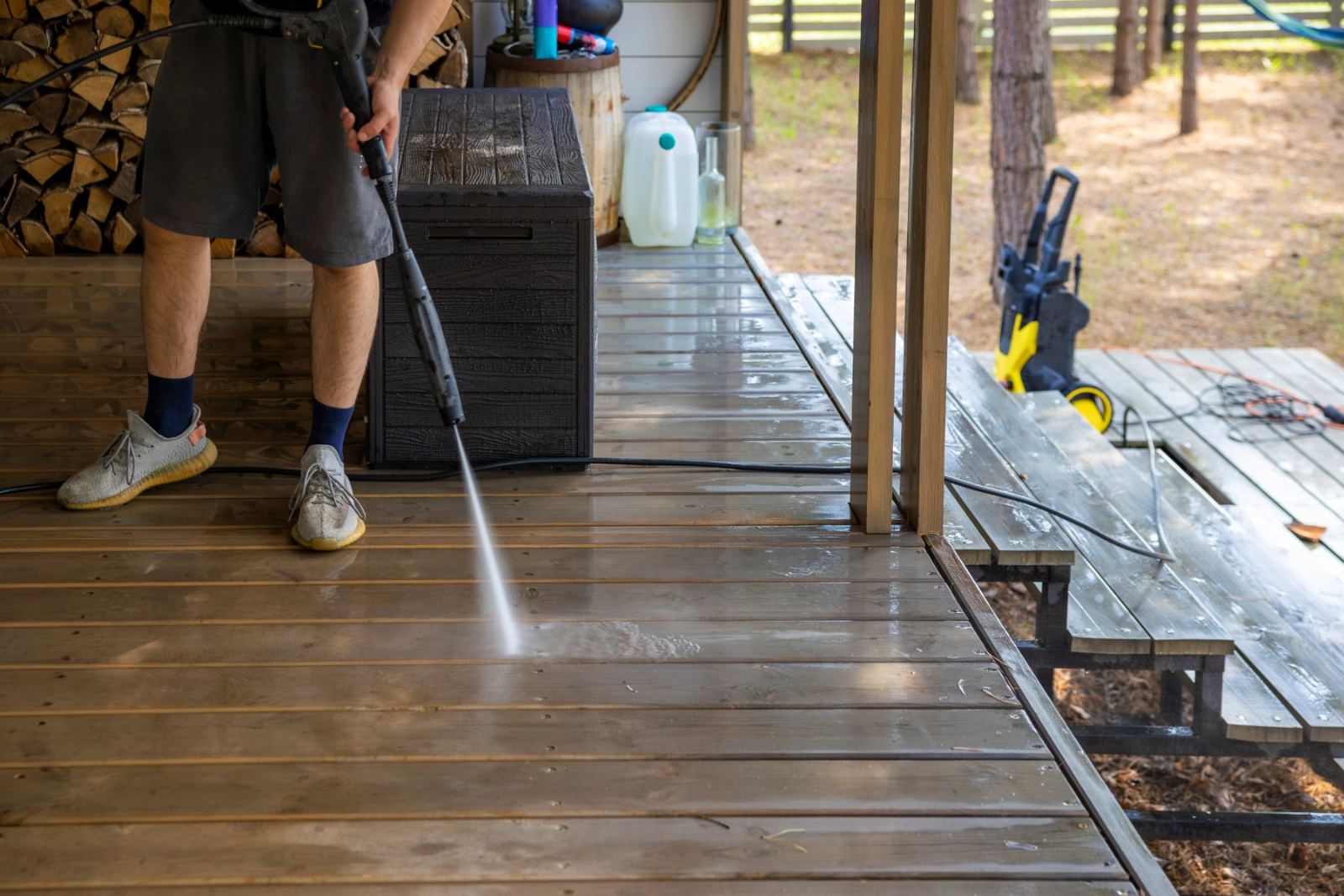 Person using pressure washer to clean wooden deck outside cabin
