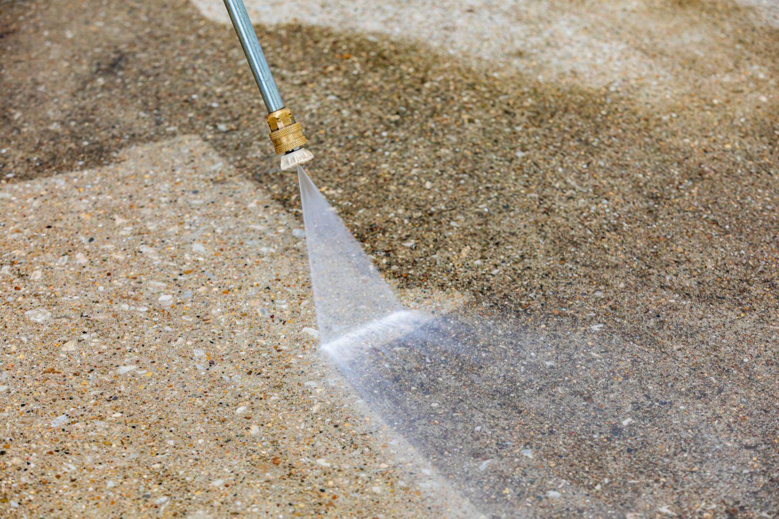 Pressure washer nozzle spraying water on concrete surface during cleaning