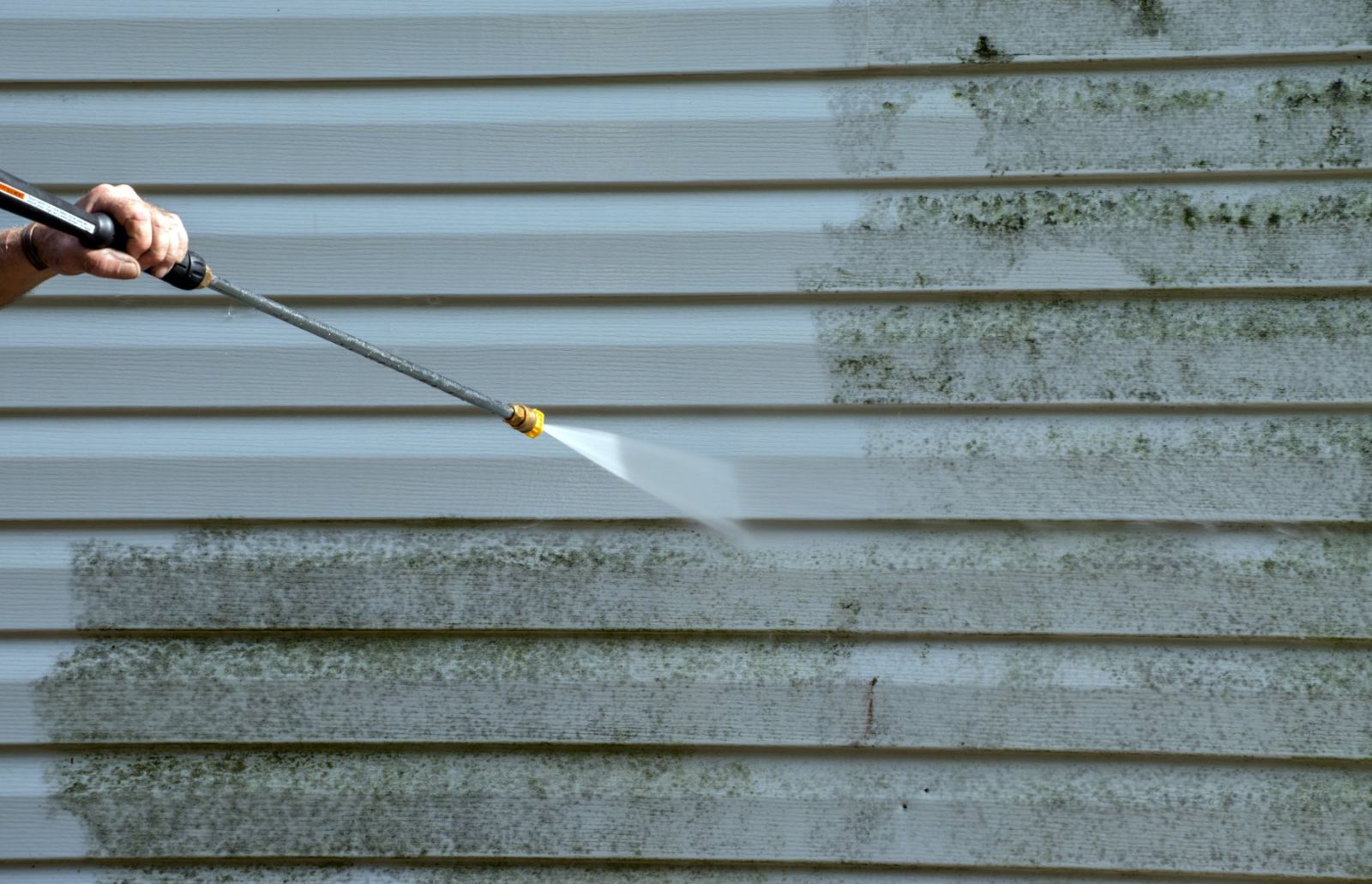 Worker pressure washing siding to remove mold and mildew buildup