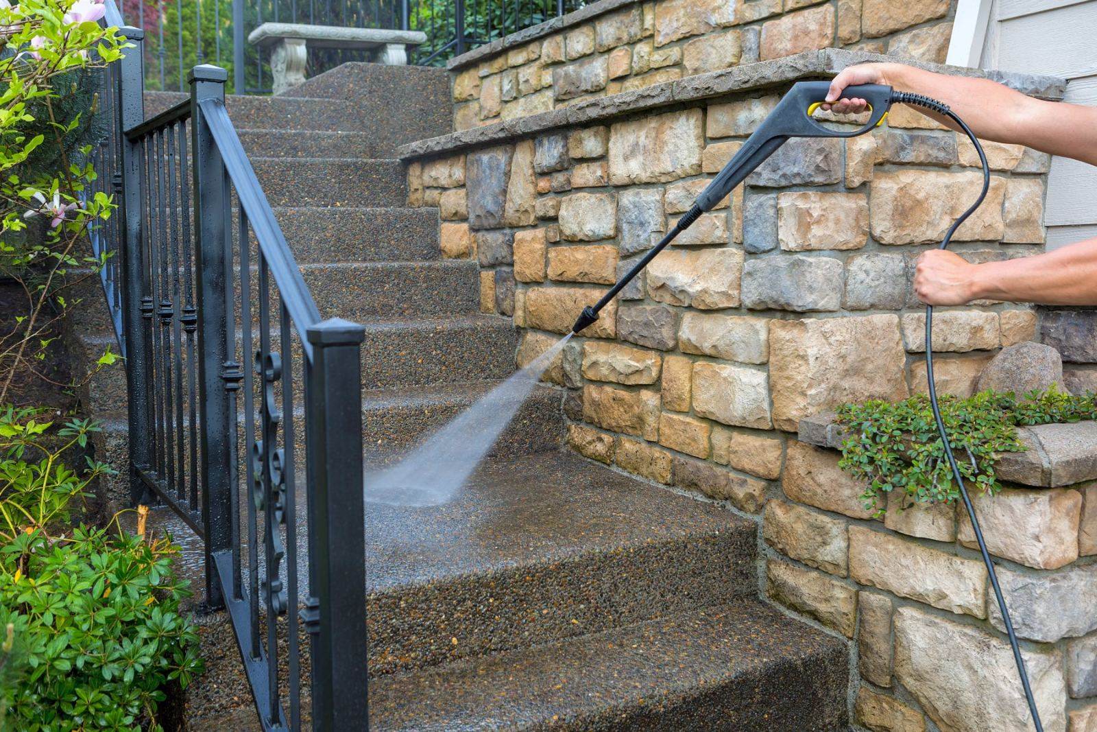 Person pressure washing a stone wall and driveway with a power washer
